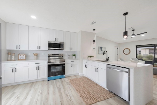 kitchen featuring white cabinets, decorative light fixtures, appliances with stainless steel finishes, sink, and kitchen peninsula