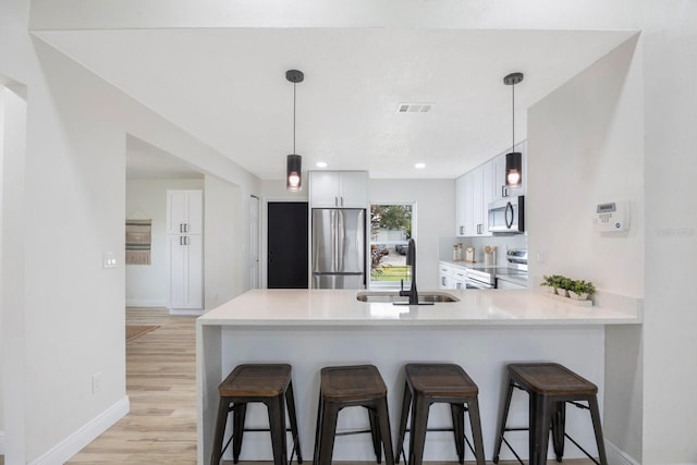 kitchen featuring white cabinetry, kitchen peninsula, sink, appliances with stainless steel finishes, and light hardwood / wood-style floors