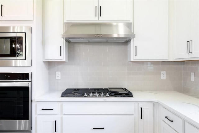 kitchen with wall chimney exhaust hood, appliances with stainless steel finishes, light stone countertops, and white cabinets