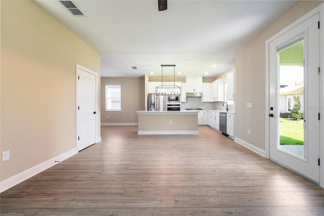 kitchen with a healthy amount of sunlight, white cabinetry, a center island, hanging light fixtures, and light hardwood / wood-style floors