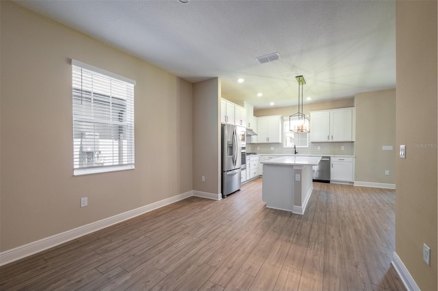 kitchen with pendant lighting, light hardwood / wood-style flooring, appliances with stainless steel finishes, and a kitchen island