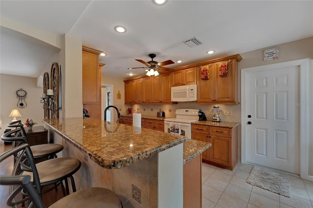 kitchen featuring kitchen peninsula, stone counters, a kitchen breakfast bar, white appliances, and ceiling fan