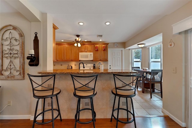 kitchen featuring light wood-type flooring, kitchen peninsula, a kitchen bar, light stone countertops, and ceiling fan