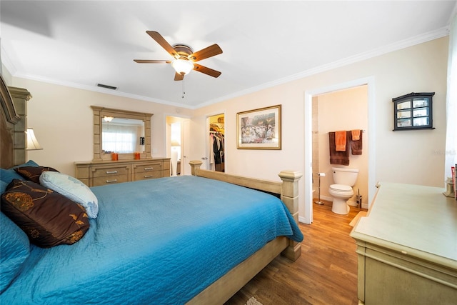 bedroom featuring a closet, hardwood / wood-style flooring, connected bathroom, a walk in closet, and crown molding