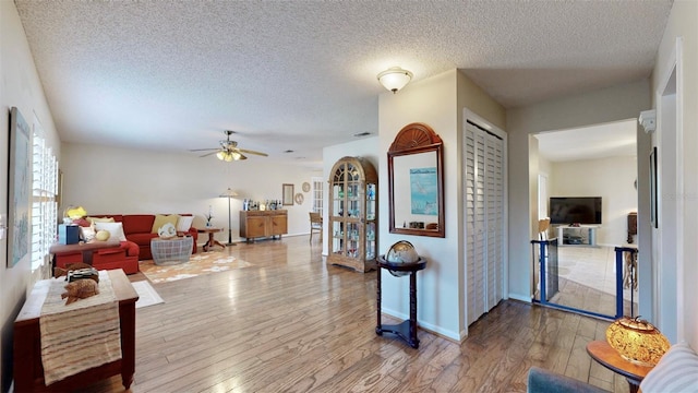 living room with a textured ceiling, ceiling fan, and wood-type flooring