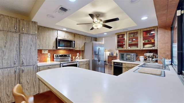 kitchen featuring kitchen peninsula, sink, ceiling fan, a tray ceiling, and appliances with stainless steel finishes