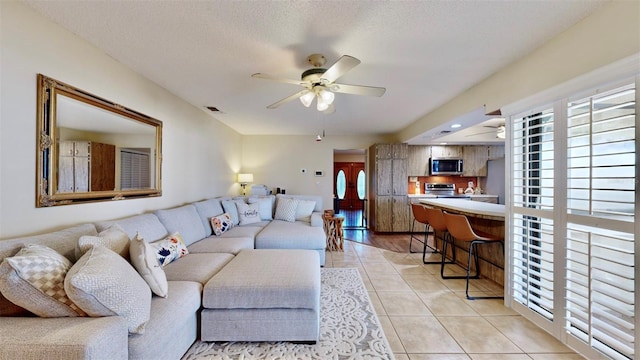 living room with light wood-type flooring, ceiling fan, and a textured ceiling