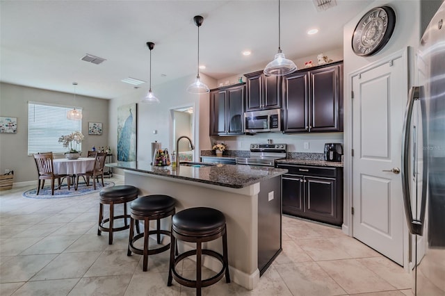 kitchen with decorative light fixtures, appliances with stainless steel finishes, sink, dark stone counters, and a kitchen island with sink