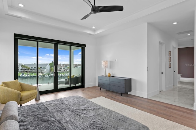 bedroom featuring french doors, access to outside, a tray ceiling, ceiling fan, and a water view