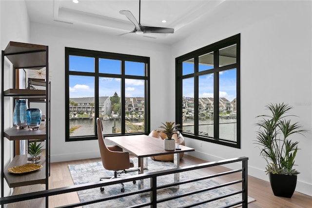 dining space with plenty of natural light, light hardwood / wood-style floors, a water view, and a tray ceiling