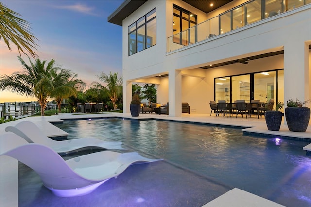 pool at dusk featuring ceiling fan and a patio