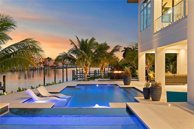 pool at dusk featuring a jacuzzi, a water view, a patio, and pool water feature