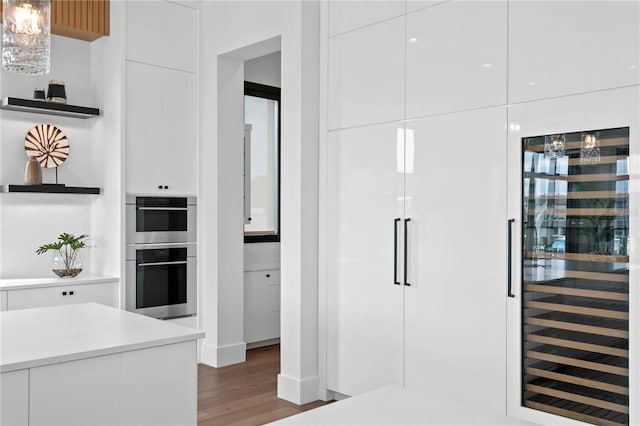 kitchen featuring dark hardwood / wood-style flooring, wine cooler, stainless steel double oven, pendant lighting, and white cabinetry