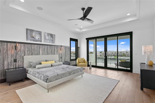 bedroom featuring access to outside, a water view, a raised ceiling, and ceiling fan