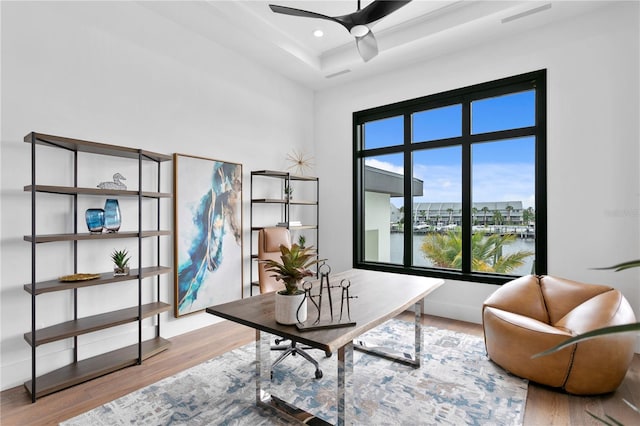 home office with a water view, ceiling fan, light hardwood / wood-style floors, and a tray ceiling