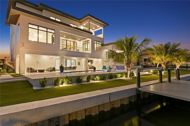 back house at dusk with a yard, an outdoor living space, a balcony, and a patio