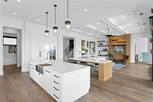 kitchen with a kitchen island with sink, coffered ceiling, white cabinets, sink, and beam ceiling