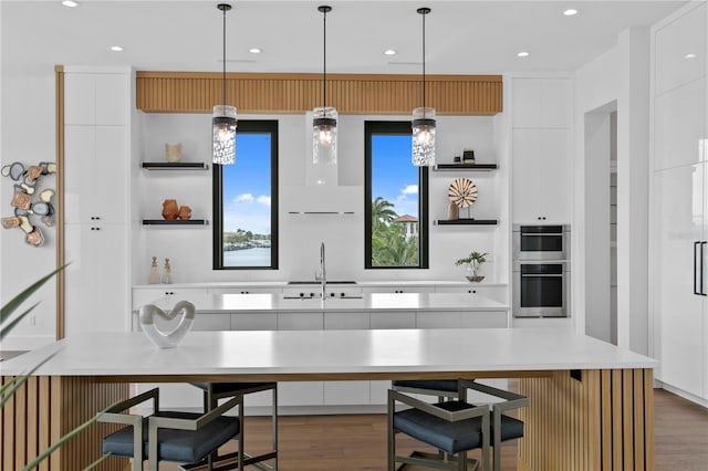 kitchen featuring double oven, white cabinetry, hanging light fixtures, and a large island