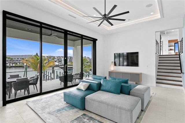 living room with ceiling fan, french doors, light tile patterned floors, a tray ceiling, and a water view