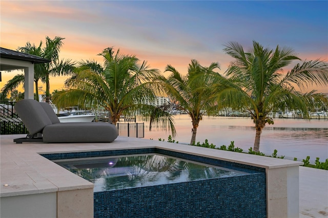 pool at dusk with a jacuzzi, a patio, and a water view