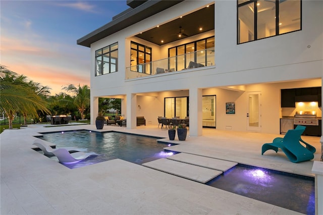 pool at dusk with an outdoor kitchen, a patio area, and a jacuzzi