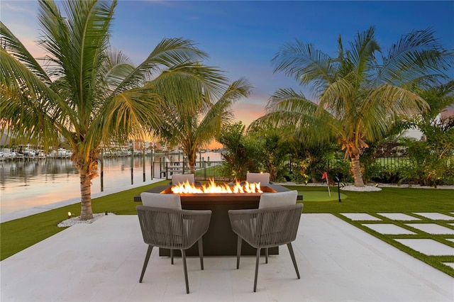 patio terrace at dusk featuring a yard, a water view, and a fire pit