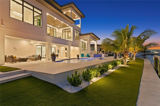 back house at dusk with outdoor lounge area, a yard, a patio, and a balcony