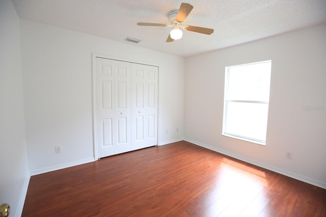 unfurnished bedroom with ceiling fan, a textured ceiling, a closet, and dark hardwood / wood-style floors