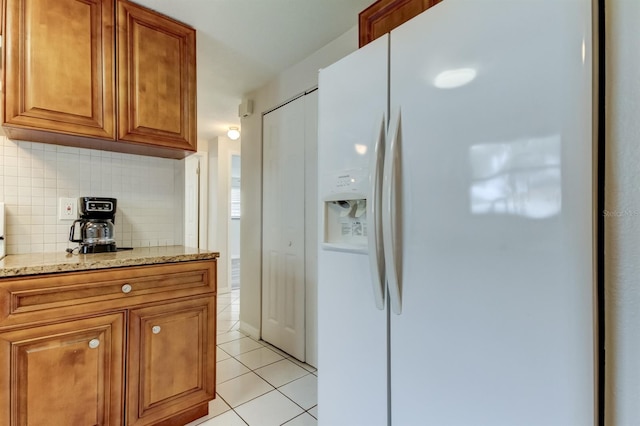 kitchen with light stone counters, light tile patterned floors, white fridge with ice dispenser, and decorative backsplash