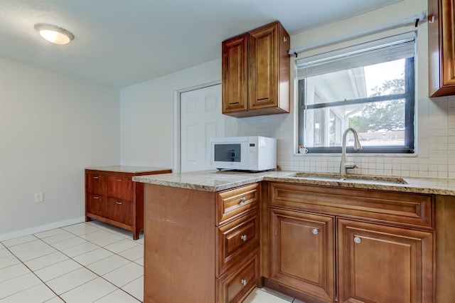 kitchen with light tile patterned flooring, kitchen peninsula, sink, and tasteful backsplash