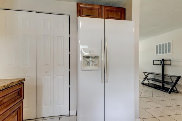 kitchen featuring light stone counters, light tile patterned floors, and white refrigerator with ice dispenser