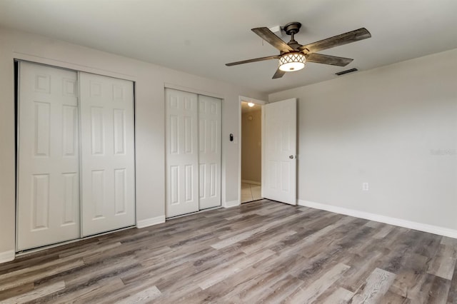 unfurnished bedroom with ceiling fan, light wood-type flooring, and two closets