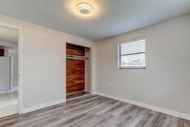 unfurnished bedroom featuring a closet, white refrigerator, and light hardwood / wood-style flooring