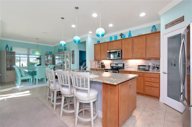 kitchen with light stone countertops, stainless steel appliances, a center island with sink, and hanging light fixtures