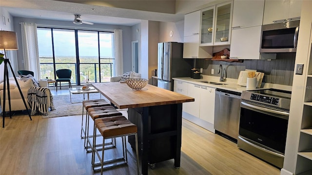 kitchen featuring light wood-type flooring, backsplash, stainless steel appliances, sink, and white cabinets