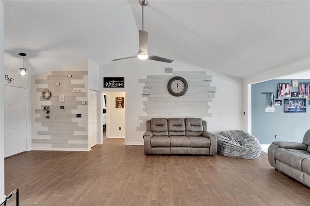 living room featuring ceiling fan, lofted ceiling, wood walls, a textured ceiling, and hardwood / wood-style floors