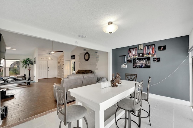 dining room featuring vaulted ceiling, a fireplace, light wood-type flooring, a textured ceiling, and ceiling fan