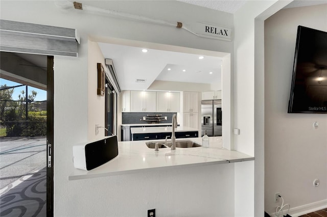 kitchen with light stone counters, white cabinets, stainless steel fridge, sink, and kitchen peninsula