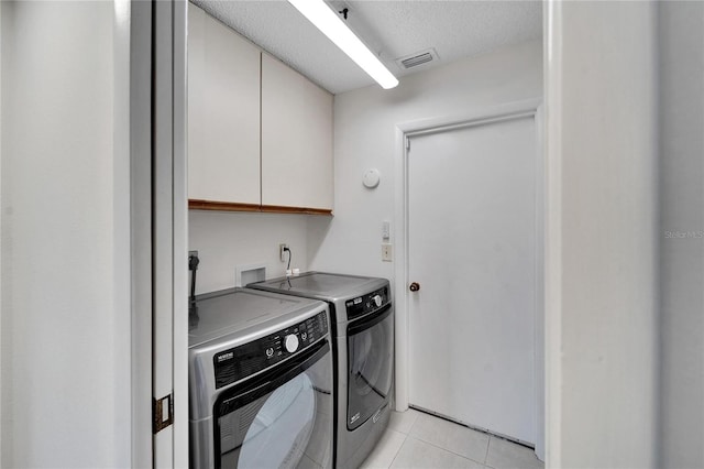 clothes washing area with a textured ceiling, washer and clothes dryer, light tile patterned floors, and cabinets