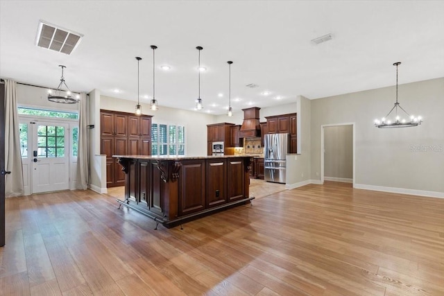 kitchen featuring stainless steel fridge, light wood-type flooring, a kitchen breakfast bar, decorative light fixtures, and a large island