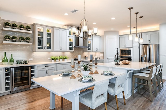 kitchen featuring a kitchen island with sink, hardwood / wood-style flooring, decorative light fixtures, and beverage cooler