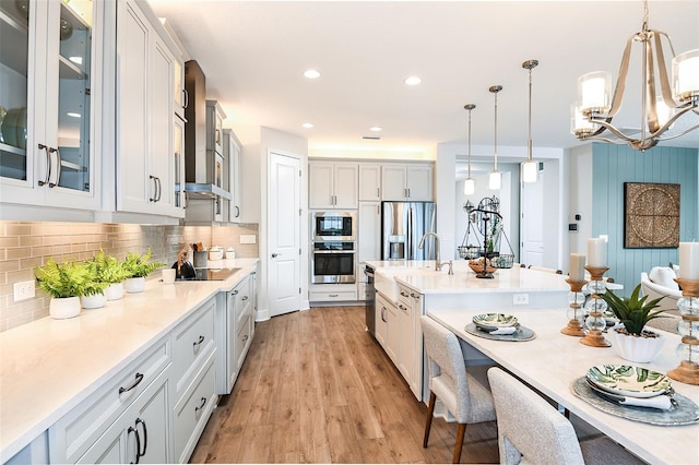 kitchen featuring white cabinets, light wood-type flooring, wall chimney exhaust hood, decorative light fixtures, and stainless steel appliances