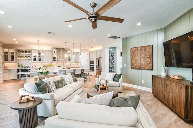 living room featuring sink, ceiling fan with notable chandelier, a textured ceiling, and light hardwood / wood-style floors