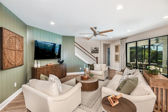 living room with a textured ceiling, hardwood / wood-style flooring, wooden walls, and ceiling fan