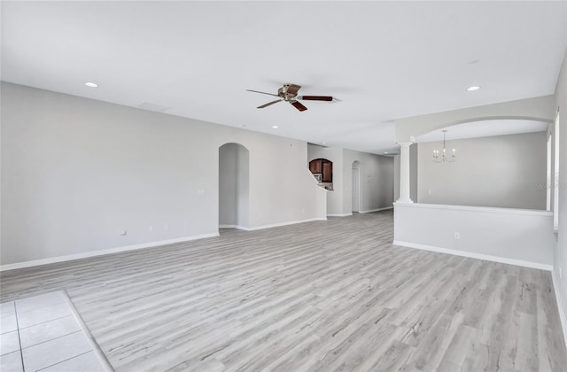 empty room with ceiling fan with notable chandelier, decorative columns, and light hardwood / wood-style floors