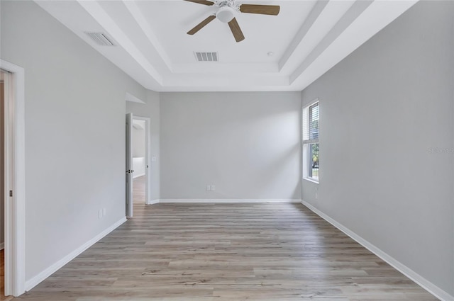 empty room with ceiling fan, light hardwood / wood-style flooring, and a raised ceiling