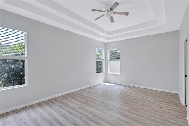 empty room featuring ceiling fan, a tray ceiling, plenty of natural light, and light hardwood / wood-style floors