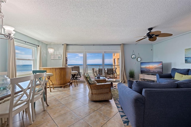 tiled living room with a water view, ceiling fan, a wealth of natural light, and a textured ceiling