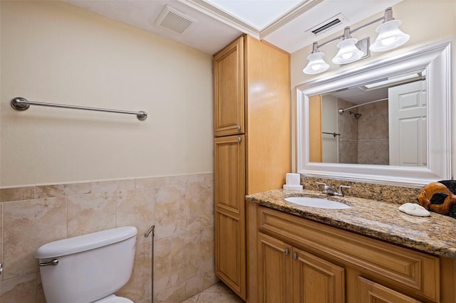 bathroom with vanity, toilet, tile walls, and a tile shower