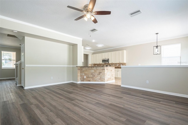 unfurnished living room with ornamental molding, dark hardwood / wood-style flooring, ceiling fan, and a textured ceiling